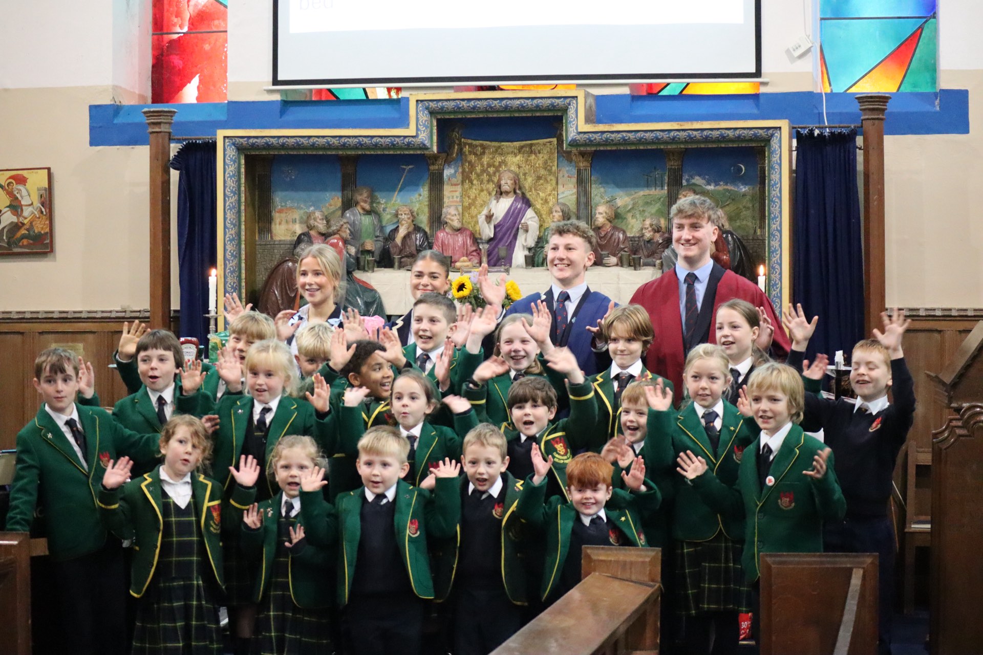 Gollop Prep School pupils waving in the College Chapel with Senior School Prefects and sunflowers behind them